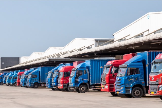 A fleet of blue and red trucks parked outside a logistics warehouse for shipping and distribution.
