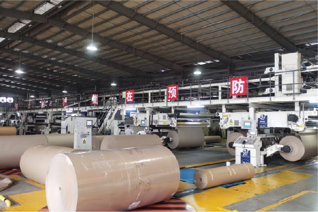 Industrial manufacturing facility with large paper rolls and automation equipment in operation.